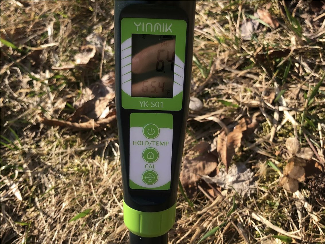 A handheld soil meter pushed into a grassy field